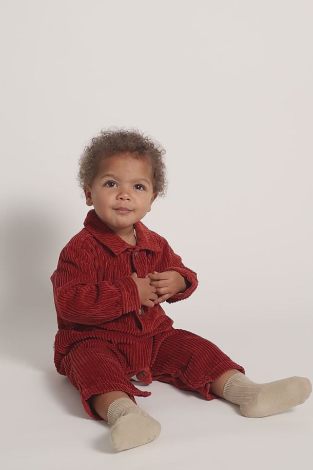 #color_ginger | Toddler boy wearing a GOTS-certified organic cotton overalls in red from cozmo
